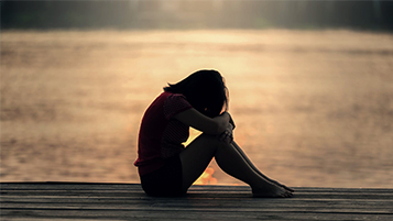 depressed woman sat on dock next to water